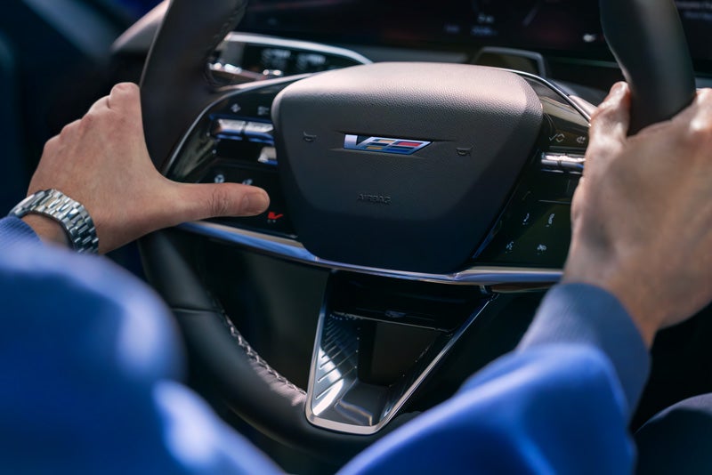 Close-up of a Man About to Press the V-Button on the 2026 OPTIQ-V Steering Wheel | Fremont Cadillac in FREMONT CA